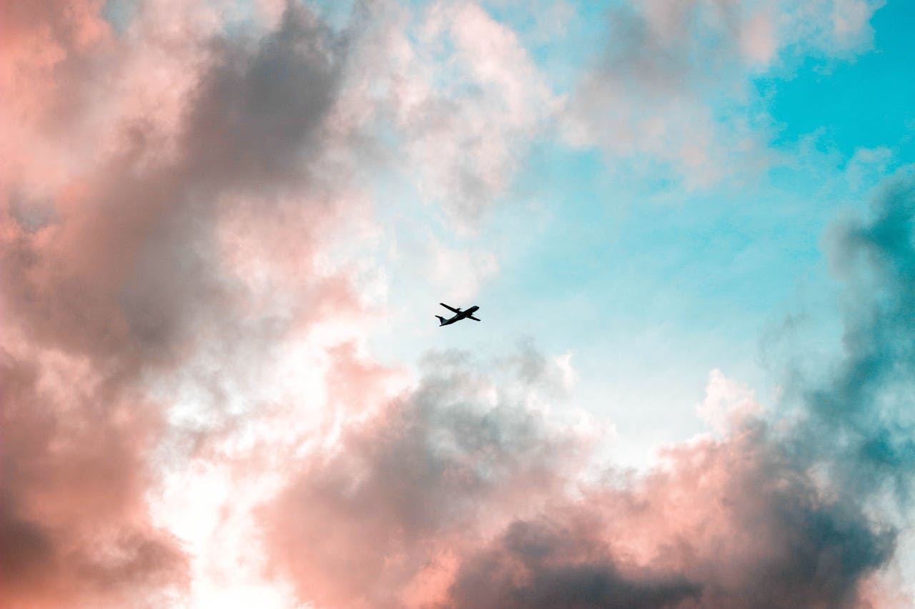 A plane flying through a colorful sky with pink and blue clouds, capturing the essence of travel.